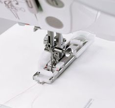 the sewing machine is on top of the white paper and threading it with scissors