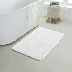 a white bath mat sitting on top of a bathroom floor next to a tub and window