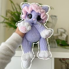 a hand holding a crocheted purple and white cat