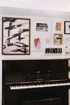 a black piano sitting in front of a white wall with pictures on the wall behind it