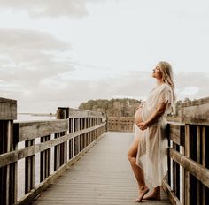 a pregnant woman standing on a wooden bridge