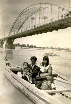 an old black and white photo of two people in a boat with a bridge in the background