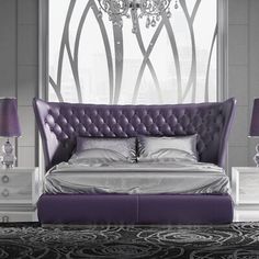 a bed with purple upholstered headboard next to two nightstands and a chandelier