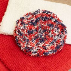 a red, white and blue knitted object sitting on top of a blanket next to a pillow