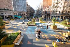 people walking and sitting on benches in the middle of a city street with painted markings