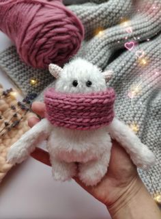 a small white stuffed animal wearing a pink knitted hat with yarn in the background