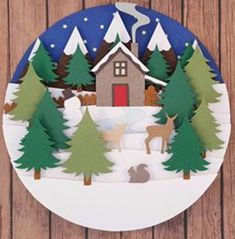 a paper cut out of a house surrounded by trees and animals in the snow on a wooden background