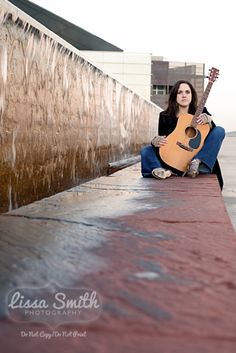 a woman sitting on the side of a building holding a guitar