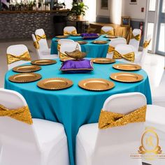 a banquet table set up with blue and gold linens, white chairs and plates