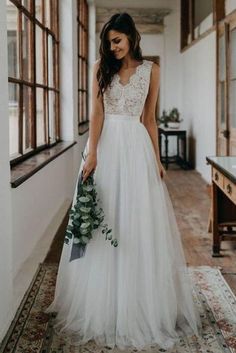 a woman in a white wedding dress holding a bouquet and looking down at the floor