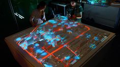 two people looking at a model of a city with neon lights on the floor and in front of them