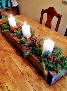 a wooden table topped with candles and greenery next to a candle holder filled with pine cones