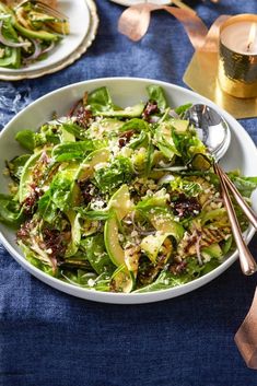 a salad with lettuce and other vegetables in a white bowl on a blue table cloth