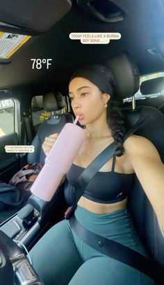 a woman sitting in the back seat of a car drinking from a pink drink bottle