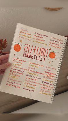 a hand holding a notebook with the words autumn bucket list written on it