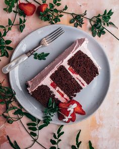 a piece of chocolate cake on a plate with strawberries and greenery around it