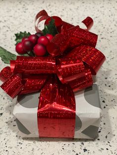 a present wrapped in red ribbon with holly and berries on the top, sitting on a table