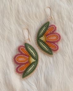 two pairs of beaded earrings with colorful flowers on them sitting on top of a white fur