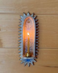 a wall mounted candle holder with a lit candle in the center on a wooden surface