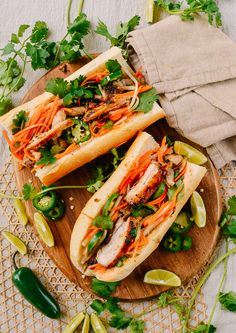 two hoagie sandwiches with carrots and cilantro on a wooden platter