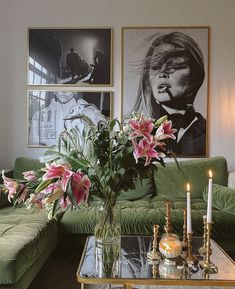 a living room with green couches and pictures on the wall above them, including flowers in vases