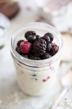 a small glass jar filled with blueberries and raspberries on top of a table