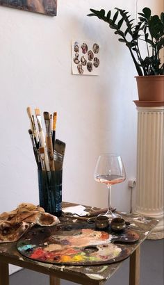 a table with paint, brushes and wine glass on it