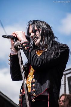 a man with black hair and makeup holding a microphone in his hand while standing on stage