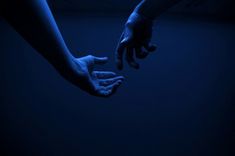 two hands reaching out to each other in the dark blue light, with one hand holding the other's hand