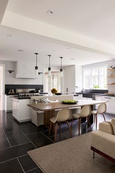 an open kitchen and living room with white walls, black tile flooring and wooden furniture