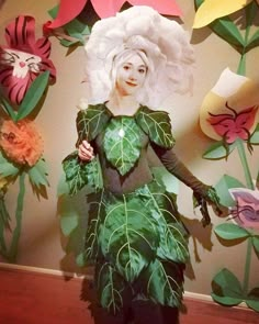 a woman dressed in green and white with flowers on the wall behind her is wearing a costume made out of paper leaves