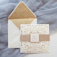 a white and gold wedding card with glitter on the front, and an envelope in the back