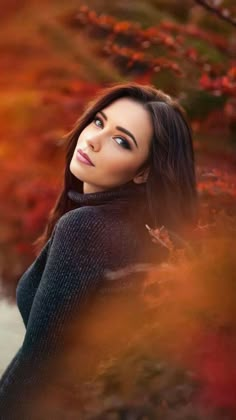 a woman with long hair standing in front of trees and looking up at the sky