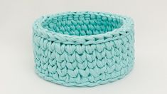 a blue basket is sitting on a white surface and it's made out of yarn