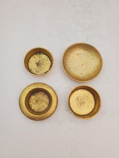 four small gold dishes are sitting on a white counter top, one is empty and the other has no food in it