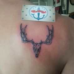 the back of a man's shoulder with an anchor and deer head tattoo on it