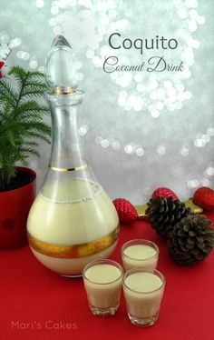 two glasses are next to a bottle of coconut drink on a red table with pine cones