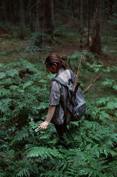 a woman with a backpack is walking through the woods and holding her hand out to reach something