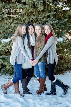 four girls standing in the snow with their arms around each other and holding hands together