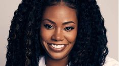 a woman with curly hair smiling at the camera, wearing a white shirt and black tie