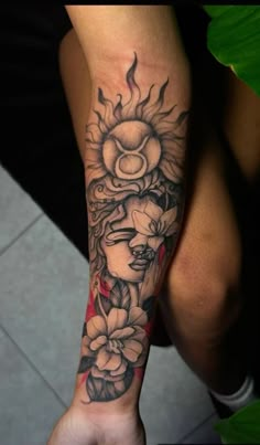 a woman's arm with flowers and sun tattoo on her left forearm, in black and grey ink