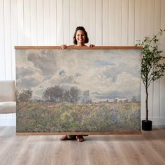 a woman holding up a large painting in front of her face