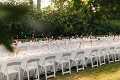 a long table is set up with white chairs and flowers in vases on the tables