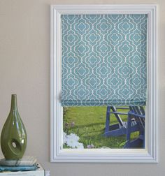 a blue and white patterned roman blind in front of a window with a green vase