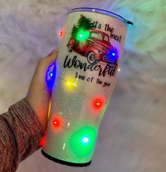 a person holding up a light up cup with christmas lights on the bottom and lettering that says it's the most wonderful time of the year