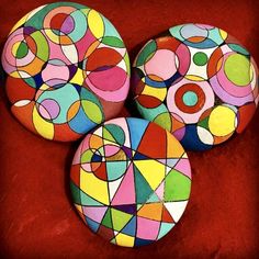 three colorfully painted rocks sitting on top of a red surface with circles in the middle