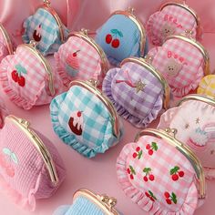 many small purses are lined up on a pink tableclothed surface, with cherries in the center