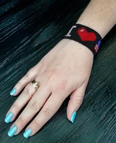 a woman's hand with blue fingernails and a red heart beaded on it