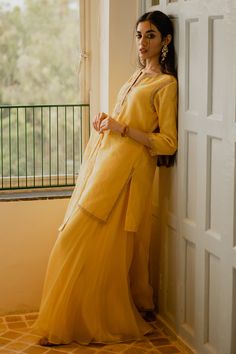 a woman standing next to a window in a yellow dress