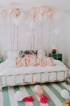 a bed with balloons on top of it and the word bride spelled out in pink